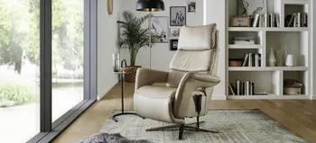 Beiger Relaxsessel mit hoher Rückenlehne und verstellbarer Funktion, modernes Wohnzimmer mit Glasfront, Teppich und stilvollen Accessoires.